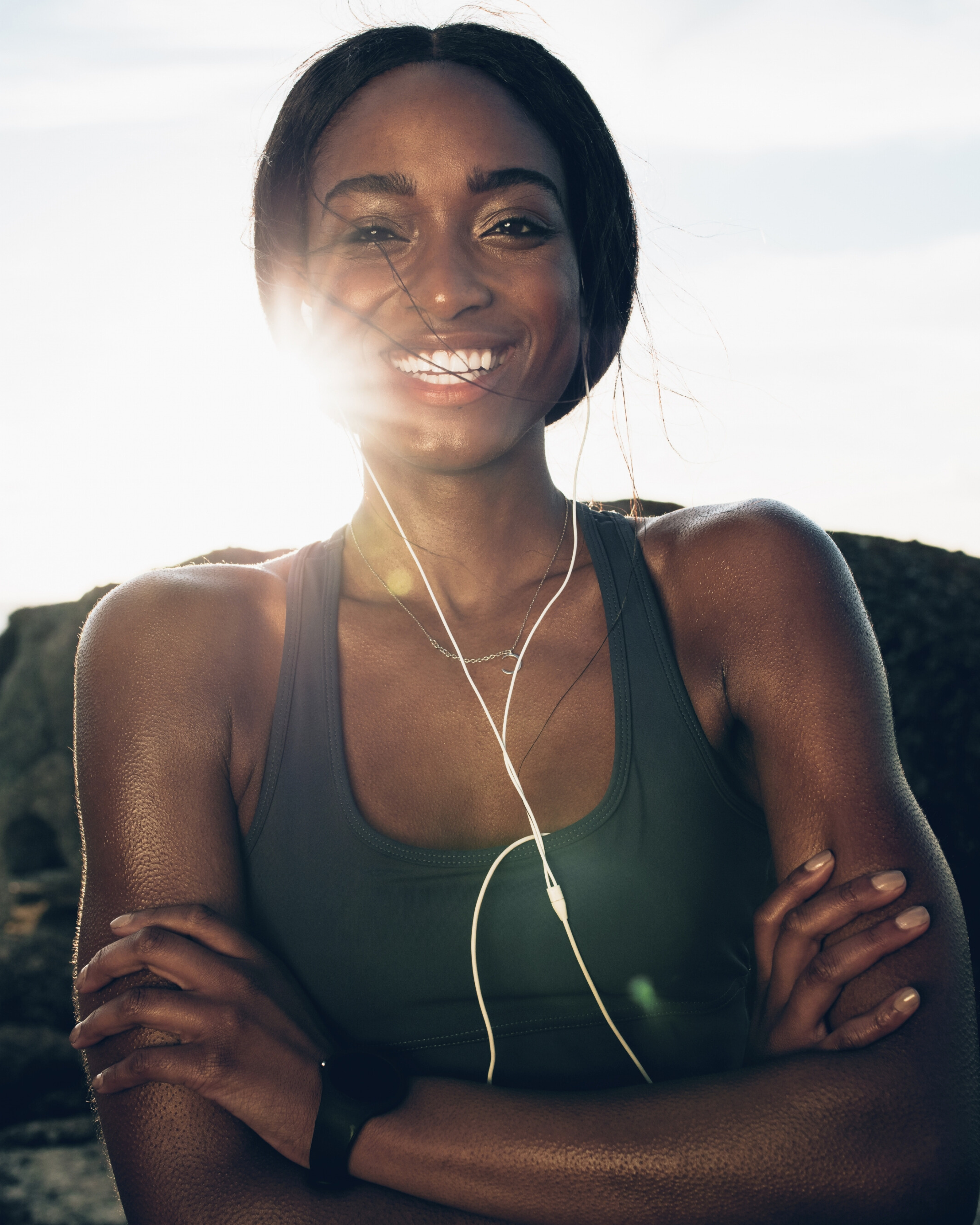Woman wearing a green tank top with earphones, standing against a neutral background