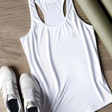Flatlay of bright white women's Ashdown t-shirt by Underscored with small Earth logo on left chest and neck branding. Shown with white sneakers and green yoga mat on wooden flooring.
