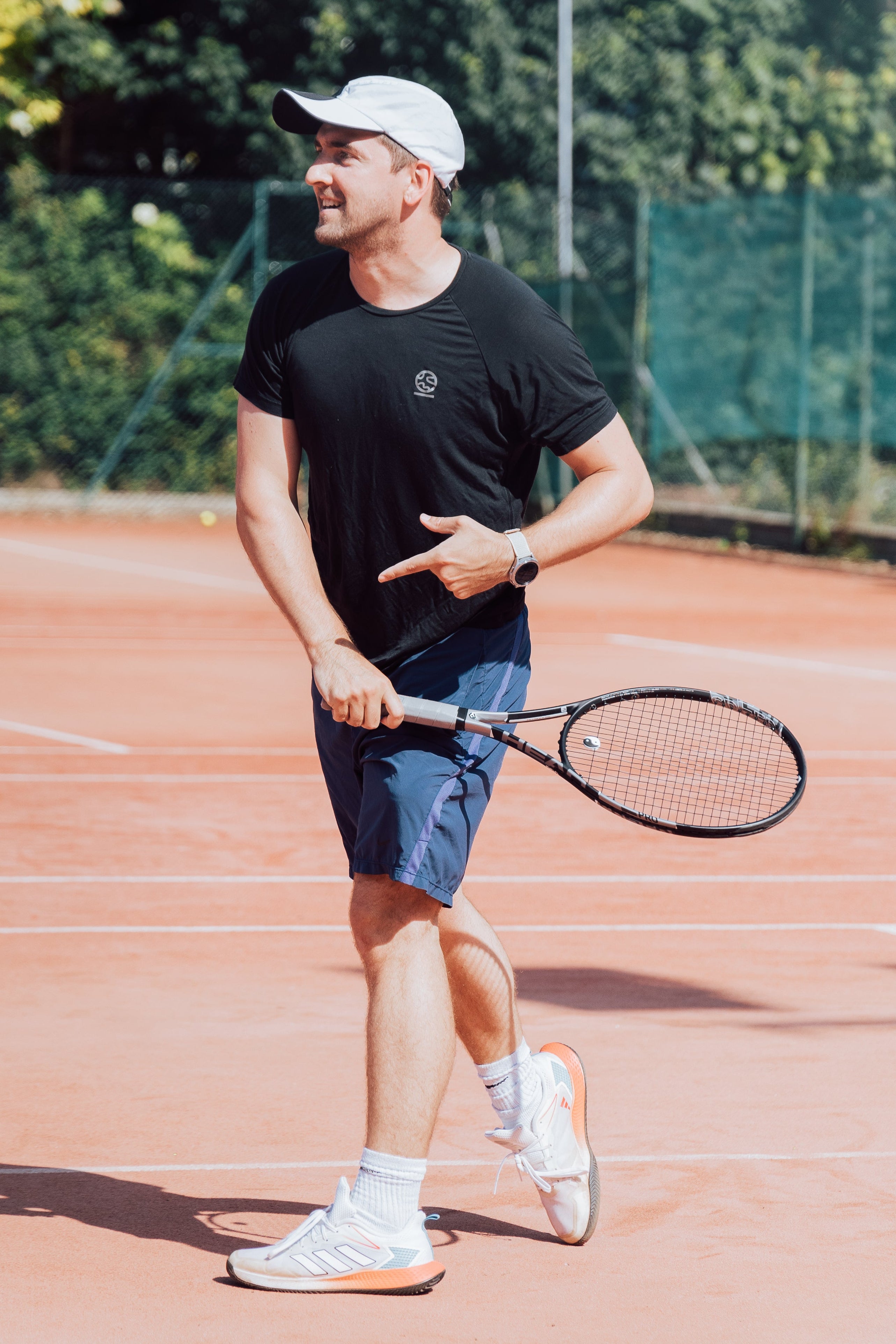 Man wearing the Underscored Men's Holmwood T-Shirt in Jet Black playing tennis on a clay court, showing the raglan sleeve design and plastic-free performance fabric in action